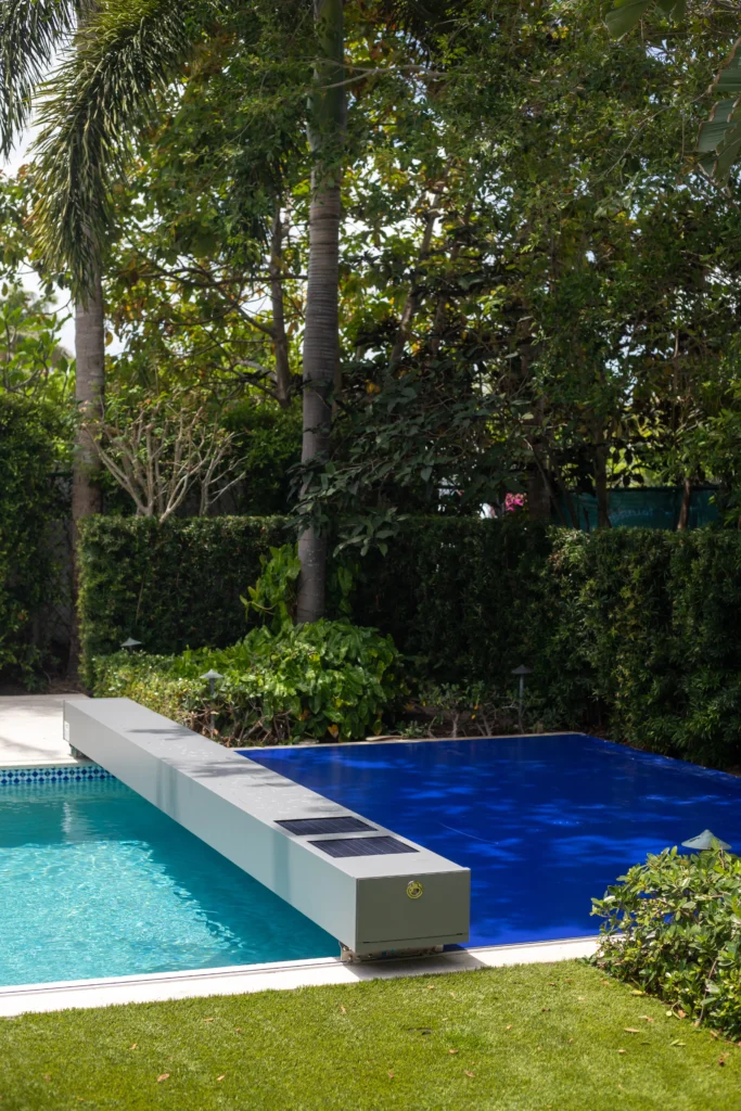 Coverseal automatic safety pool cover closed over a blue backyard pool surrounded by green landscaping