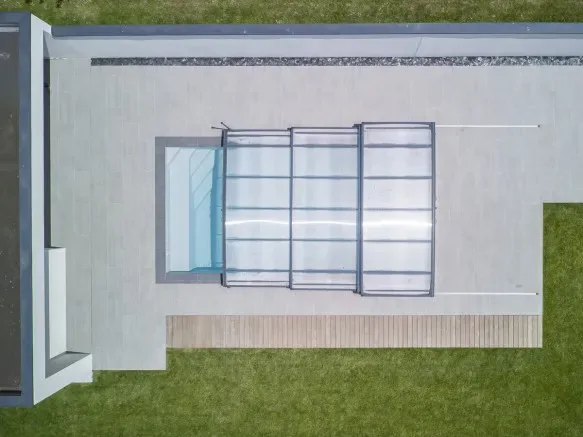 Aerial drone view of N-CLOSURE retractable pool enclosure partially closed over a modern backyard pool