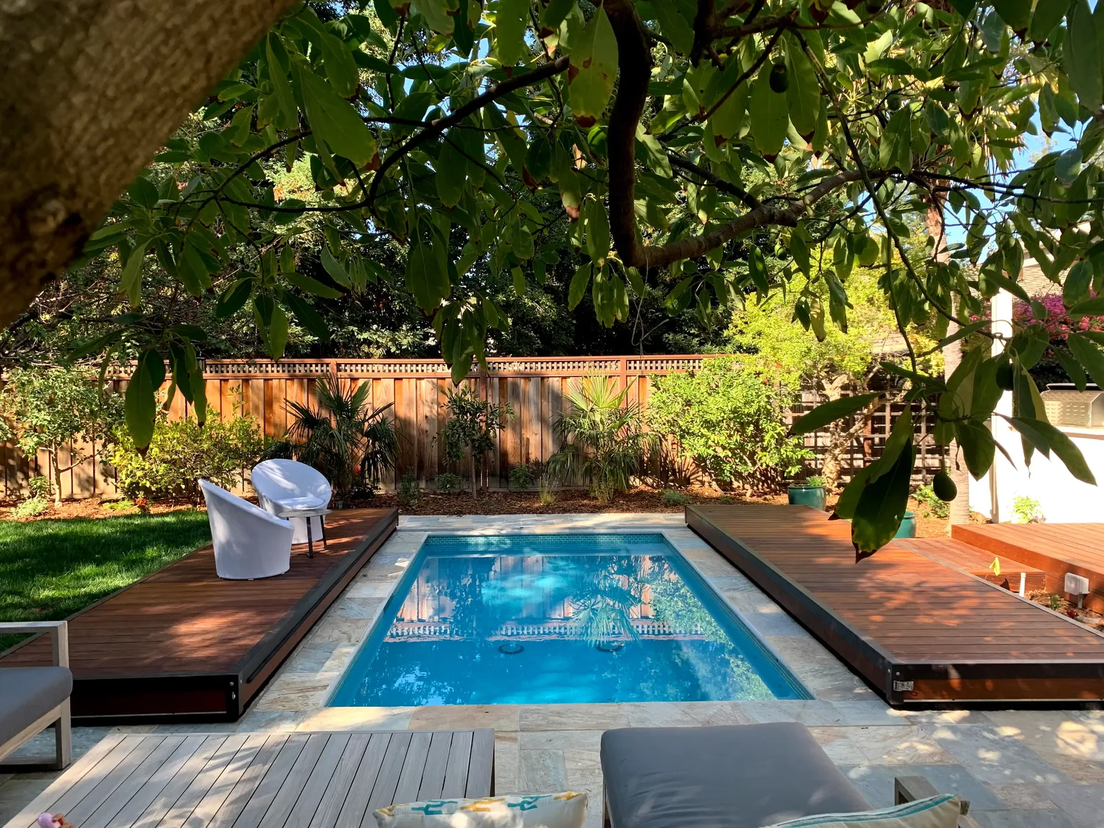 S-LIDE sliding deck pool cover with both deck platforms retracted, revealing the pool in a lush modern backyard